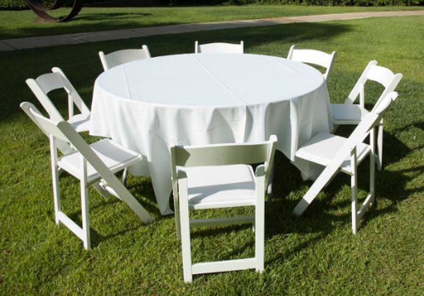 A round table under a white linen with eight white folding chairs on a lawn