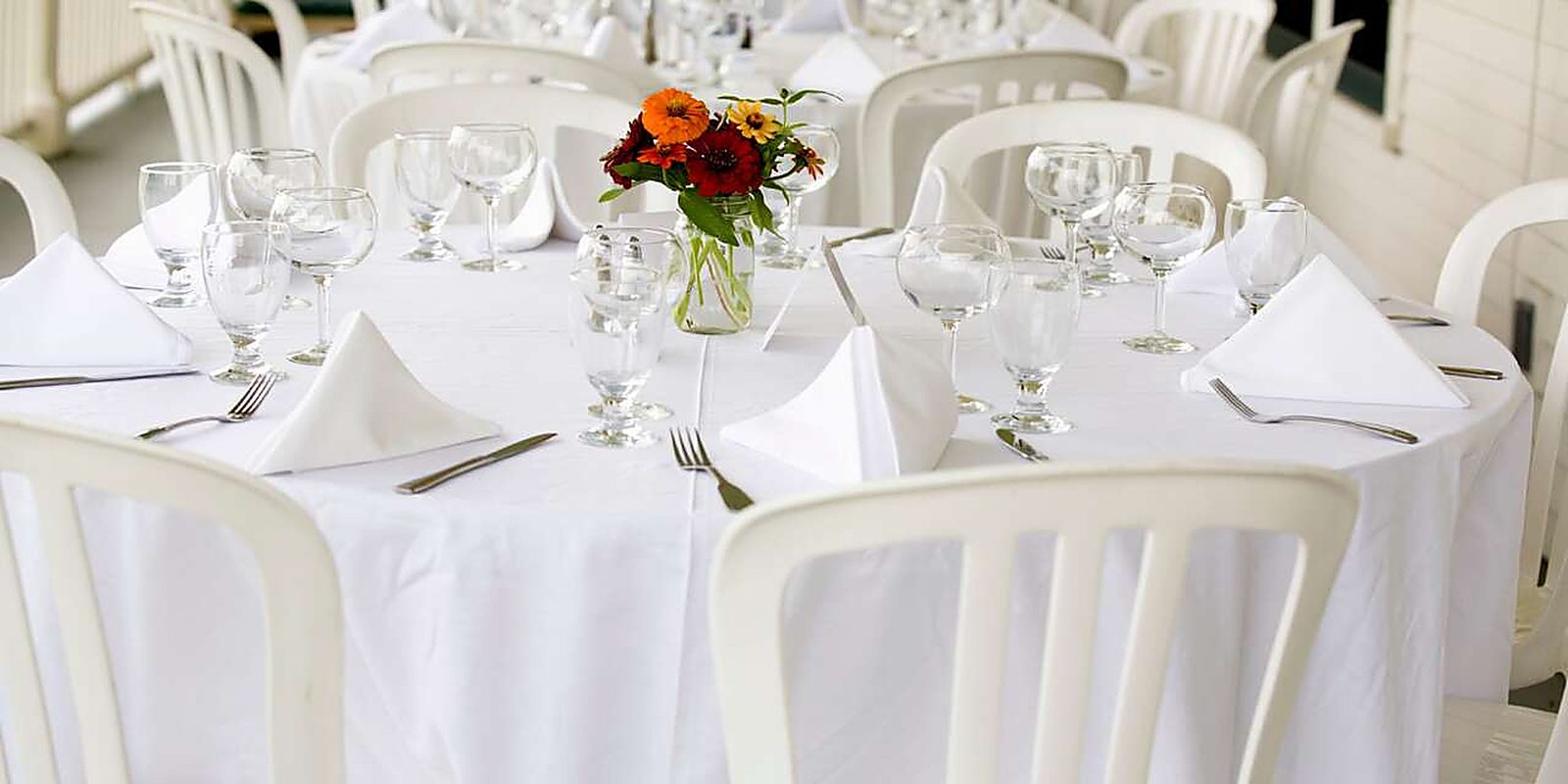 A round table under a white linen, set with glassware and folded napkins