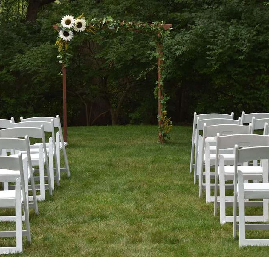 An outdoor ceremony set with our white folding chairs facing a floral arch